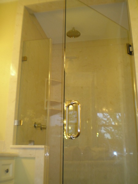 Bathroom Remodeling New Walk-In Shower with Beige Tiles. Bronze Colored Ceiling Mounted Showerhead. and Hardware. Glass Door with Brass Handle